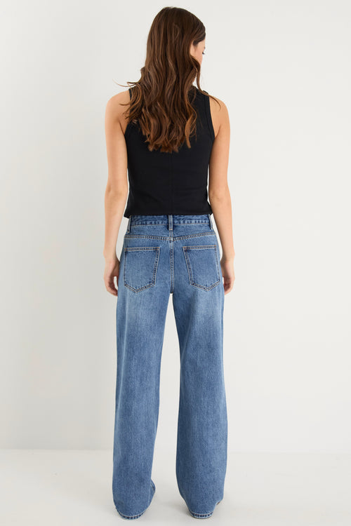 model wears a mid rise blue jean with a black tank top 