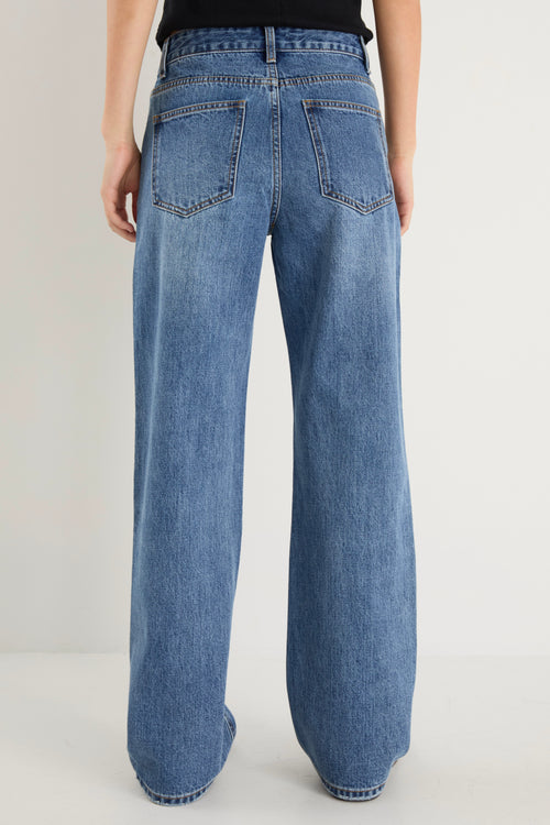 model wears a mid rise blue jean with a black tank top 