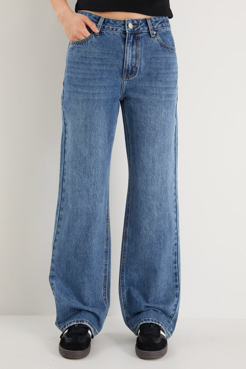 model wears a mid rise blue jean with a black tank top 