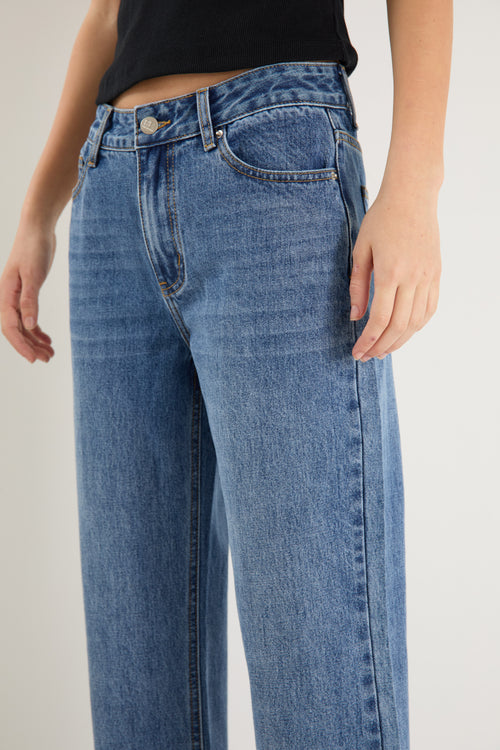 model wears a mid rise blue jean with a black tank top 