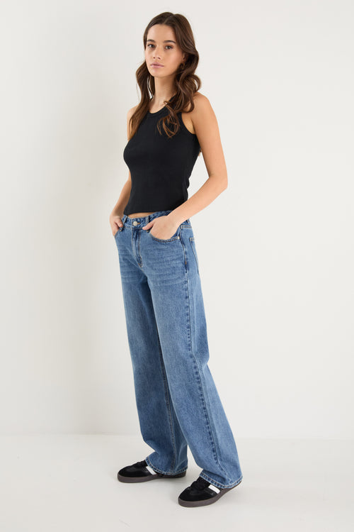 model wears a mid rise blue jean with a black tank top 