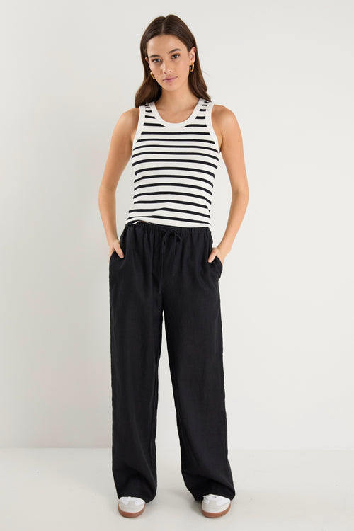 Woman wearing black wide-leg linen pants with an elasticated waistband, styled with a black and white striped tank and white sneakers.