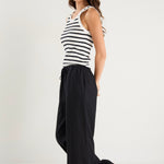 Woman wearing black wide-leg linen pants with an elasticated waistband, styled with a black and white striped tank and white sneakers.