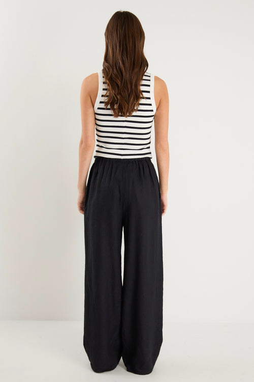 Woman wearing black wide-leg linen pants with an elasticated waistband, styled with a black and white striped tank and white sneakers.