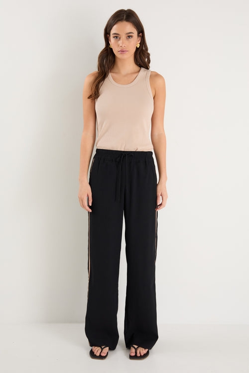 Woman wearing a beige tank top and black pants on a white background