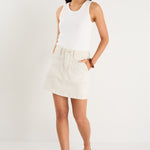 model wears a ecru denim mini skirt with a white tank top 