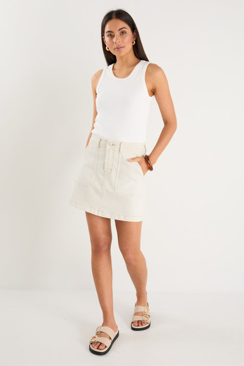 model wears a ecru denim mini skirt with a white tank top 