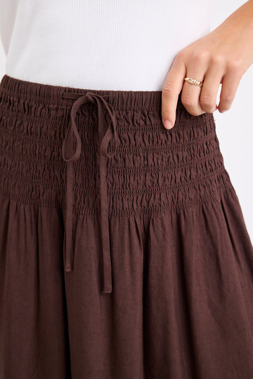model wears a brown linen maxi skirt with a white tank top