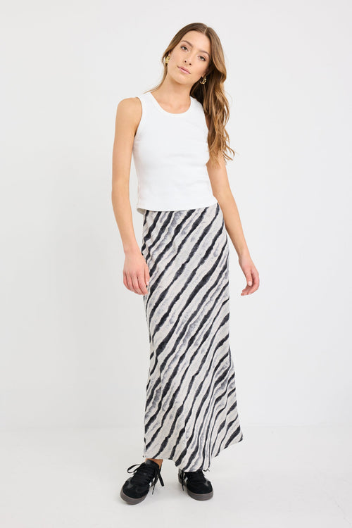 Woman wearing a white sleeveless top and black and white striped skirt on a white background
