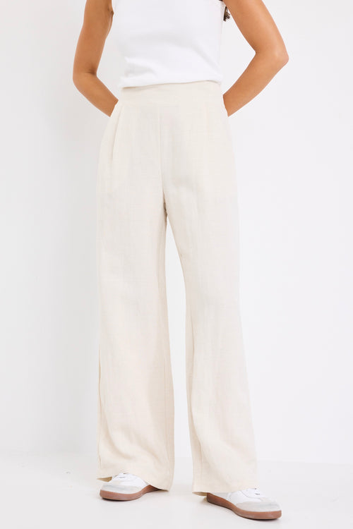 model wears a beige linen pair of pants with a white singlet