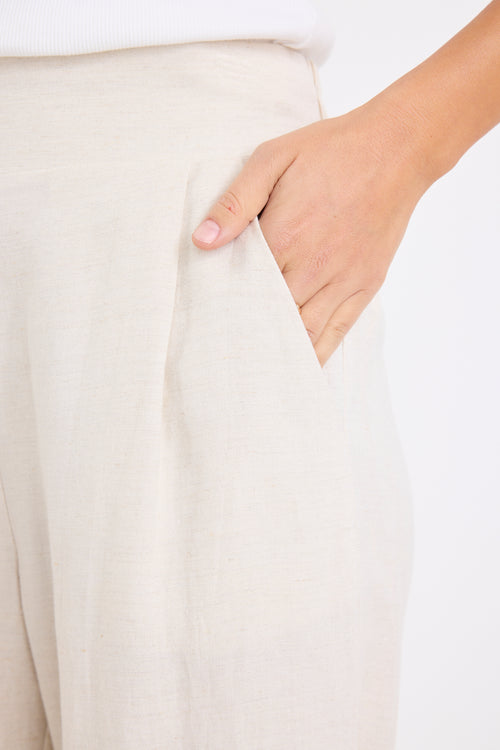 model wears a beige linen pair of pants with a white singlet