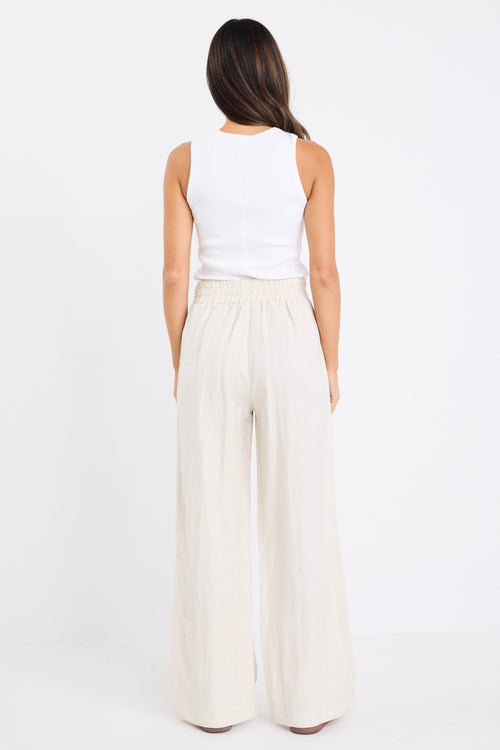 model wears a beige linen pair of pants with a white singlet