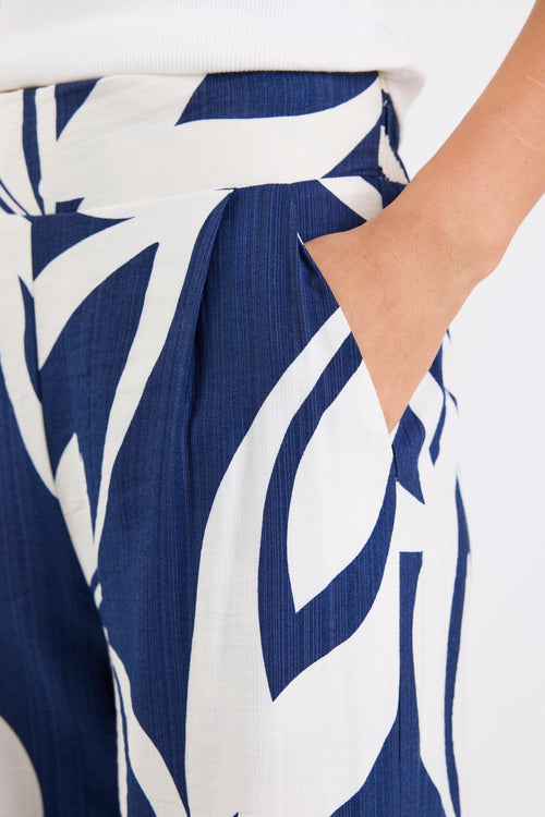 Woman wearing navy and white printed wide leg pants with an elastic waistband and high-rise fit, paired with a white tank top.