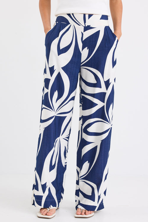 Woman wearing navy and white printed wide leg pants with an elastic waistband and high-rise fit, paired with a white tank top.