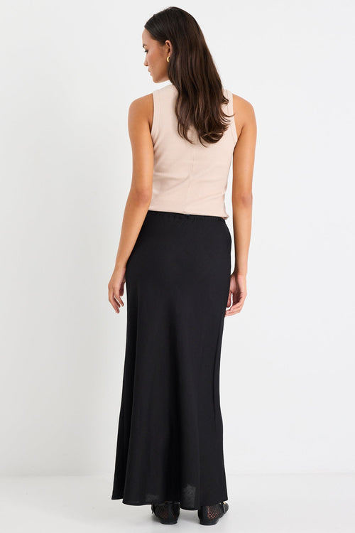 Woman wearing a beige sleeveless top and black long skirt on a white background