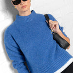 Woman wearing a blue sweater and sunglasses against a white background