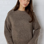 Woman wearing a brown sweater against a white brick wall