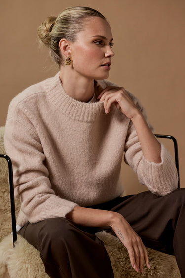 Woman wearing a beige sweater sitting on a textured surface with a neutral background
