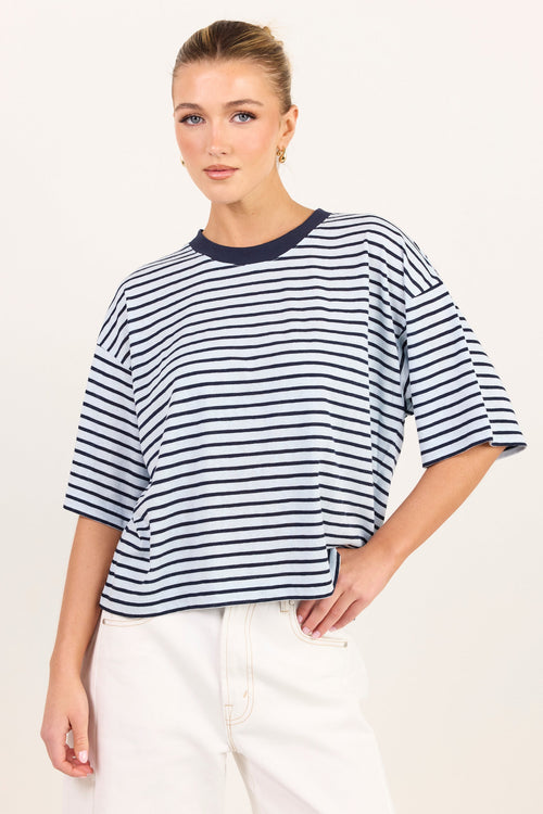 A woman modeling a short-sleeve striped t-shirt with navy blue horizontal stripes on a white background, paired with white pants.