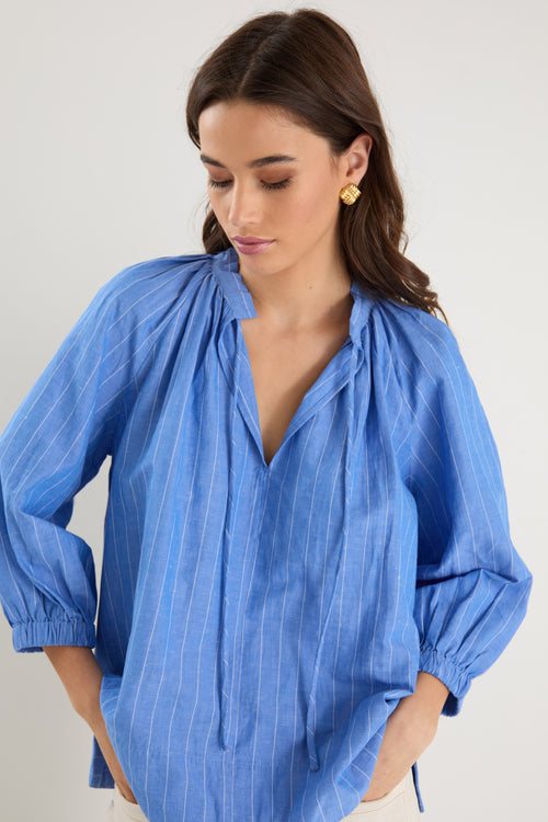 Woman wearing a relaxed-fit, blue pinstripe top with mid sleeves and a split neckline, styled with off-white jeans.