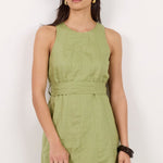 A woman modeling a sleeveless olive green linen dress with a matching fabric belt, styled with dark sunglasses and black sandals against a plain white studio background.