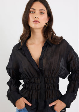 Woman wearing a black sheer blouse with long sleeves on a white background