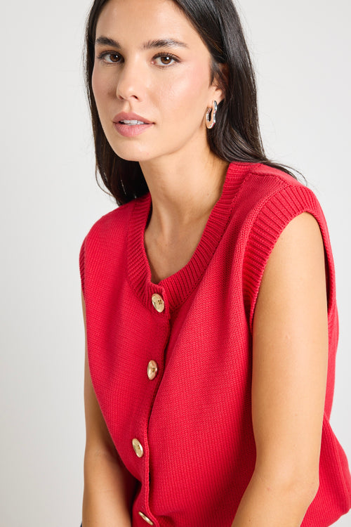 Model wears a cherry red knit vest with gold buttons. 