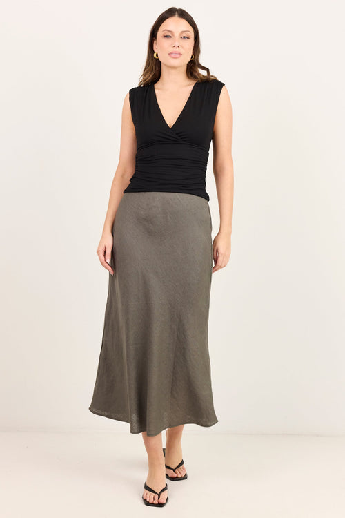 A woman modeling a sleeveless black wrap-style top and a long, flowing olive-gray skirt against a plain off-white studio background.
