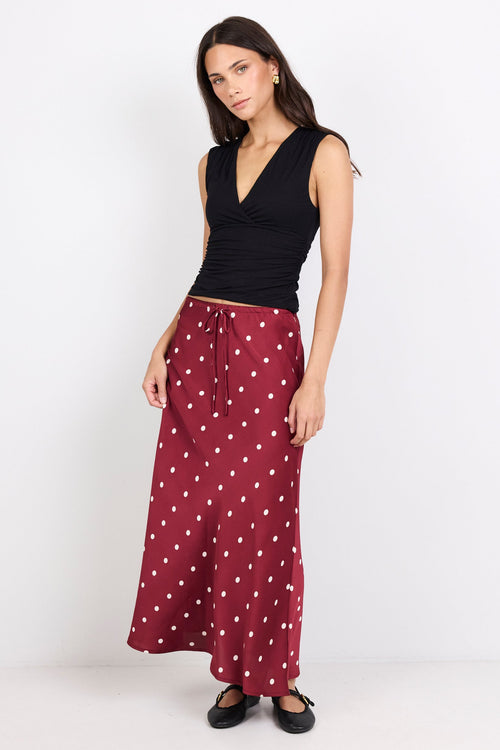 Woman wearing a black sleeveless top and red polka dot skirt on a white background