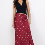 Woman wearing a black top and maroon skirt with white polka dots on a white background
