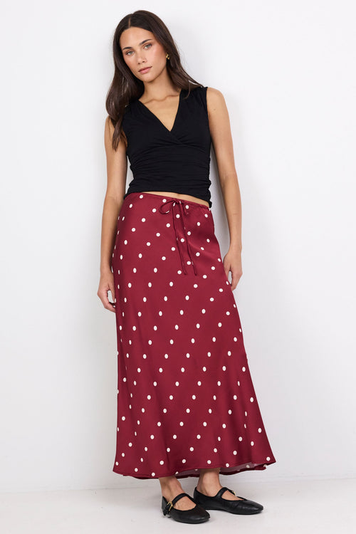 Woman wearing a black top and maroon skirt with white polka dots on a white background