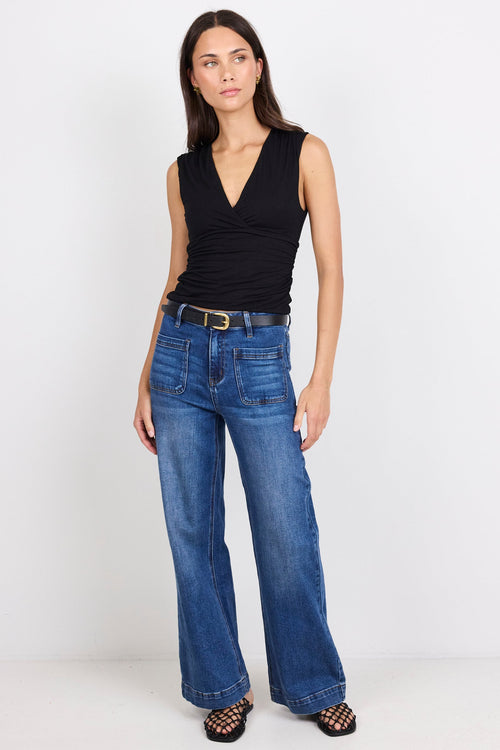 Woman wearing a black sleeveless top and blue jeans on a white background