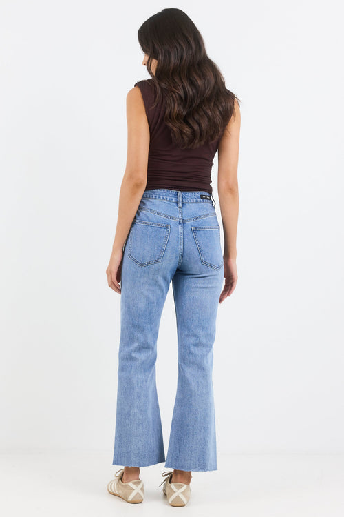 Woman wearing light blue jeans and a brown top on a white background