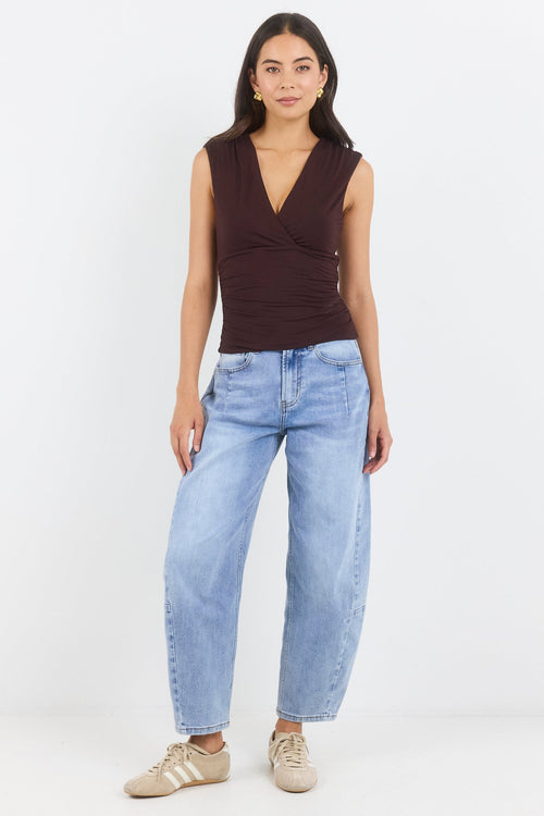 Woman wearing a brown sleeveless top and light blue jeans on a white background