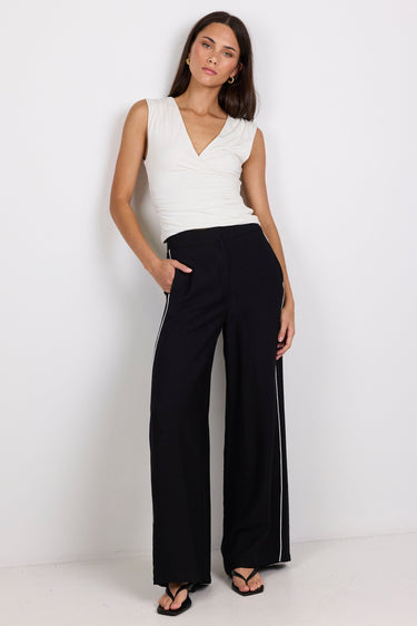 Woman wearing a white sleeveless top and black pants on a white background