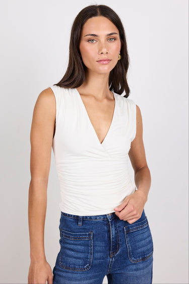 Woman wearing a white sleeveless top and blue jeans against a plain background