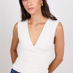 Woman wearing a white sleeveless top and blue jeans against a plain background