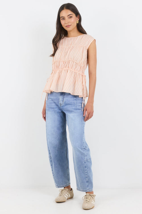 Woman wearing a light pink sleeveless top and blue jeans on a white background