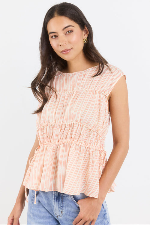 Woman wearing a peach striped top and blue jeans on a white background