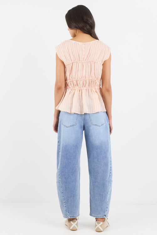 Woman wearing a light pink top and blue jeans on a white background