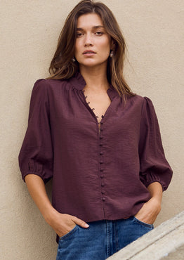 Woman standing against a beige wall with a stone wall in the foreground