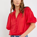 Woman wearing a red blouse with puffed sleeves and blue jeans on a white background