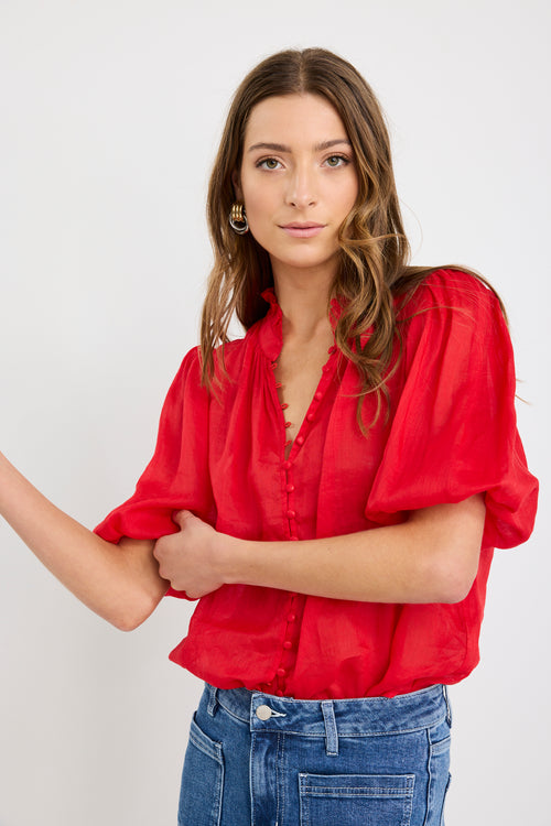 Woman wearing a red blouse and blue jeans against a white background