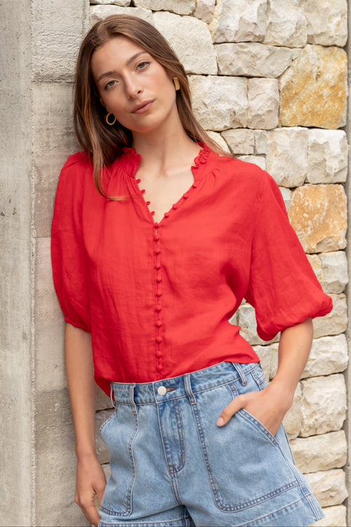 Woman wearing a red blouse and blue jeans against a stone wall.