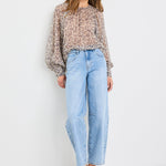 Woman wearing a patterned blouse and light blue jeans on a white background