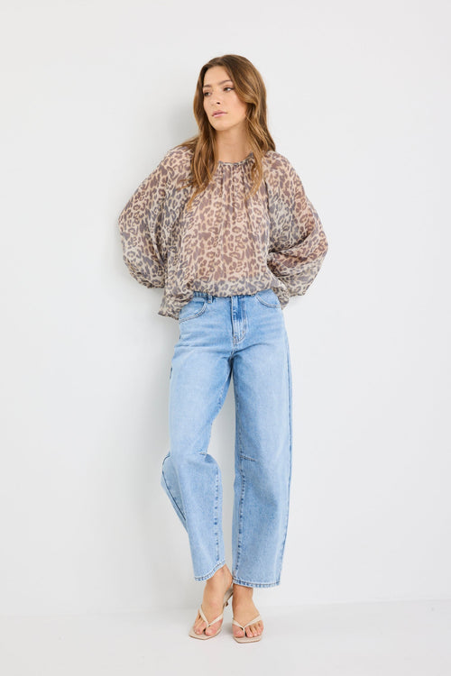 Woman wearing a patterned blouse and light blue jeans on a white background