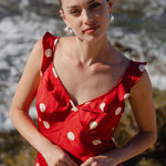 Woman wearing a red polka dot top and white pants standing by the ocean.