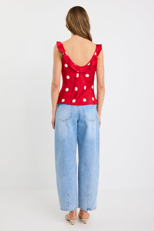 Woman wearing a cherry red polka dot cami top with ruffle neckline and tie straps, styled with light-wash wide-leg jeans.