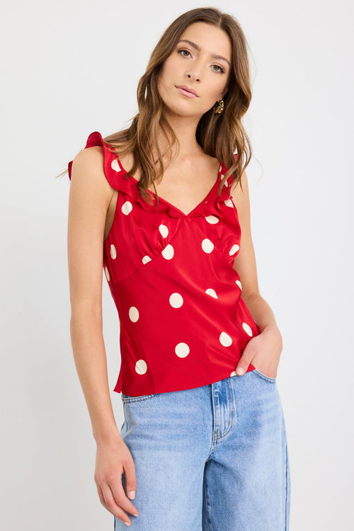 Woman wearing a cherry red polka dot cami top with ruffle neckline and tie straps, styled with light-wash wide-leg jeans.