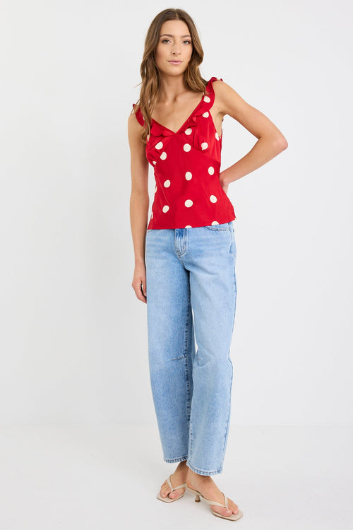 Woman wearing a red polka dot top and light blue jeans on a white background